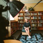 woman sitting on armless chair with light between bookcases in room
